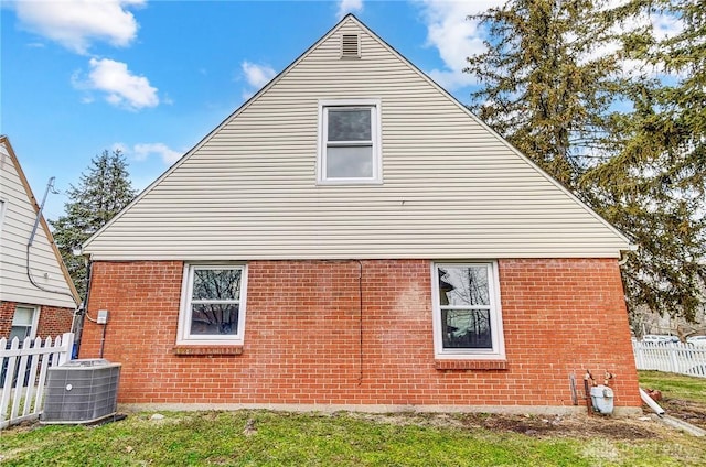 view of side of home featuring cooling unit, brick siding, and fence