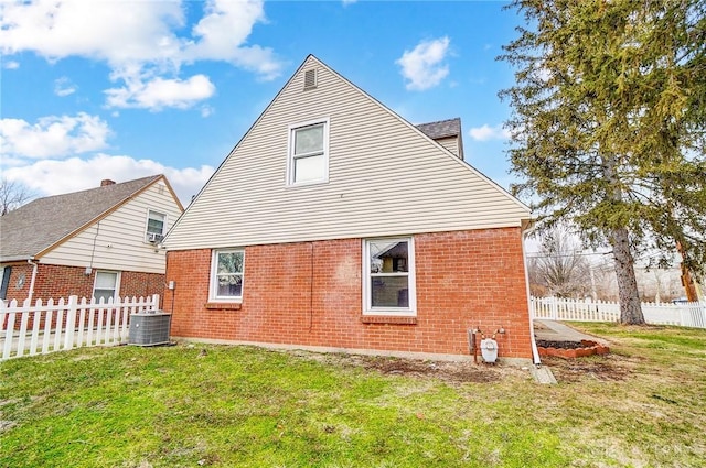 rear view of house featuring a yard, brick siding, cooling unit, and fence