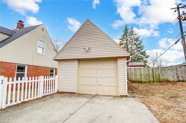 detached garage featuring concrete driveway and fence