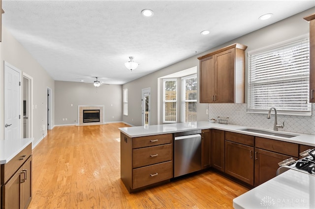 kitchen with light countertops, a tiled fireplace, appliances with stainless steel finishes, a sink, and a peninsula