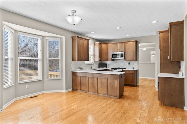 kitchen with a peninsula, light wood finished floors, plenty of natural light, and stainless steel microwave