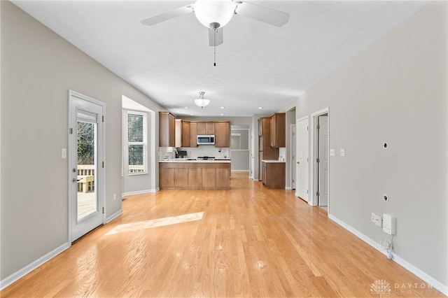 kitchen with a peninsula, open floor plan, light countertops, brown cabinets, and stainless steel microwave