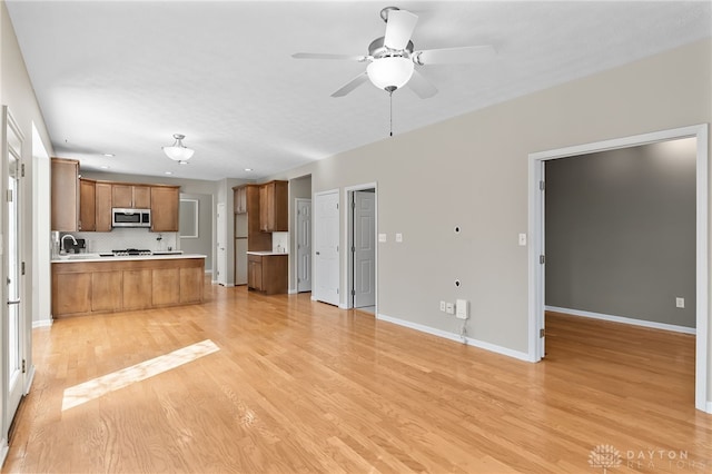 kitchen with light wood-style floors, open floor plan, light countertops, brown cabinets, and stainless steel microwave