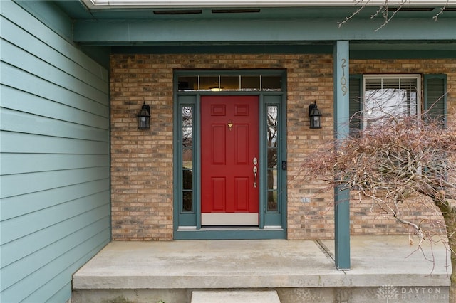 doorway to property featuring a porch and brick siding