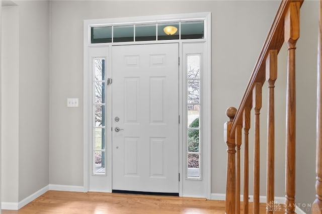 foyer entrance featuring light wood-type flooring, stairway, and baseboards