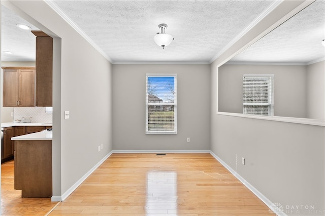 unfurnished dining area featuring light wood-style floors, baseboards, a textured ceiling, and ornamental molding