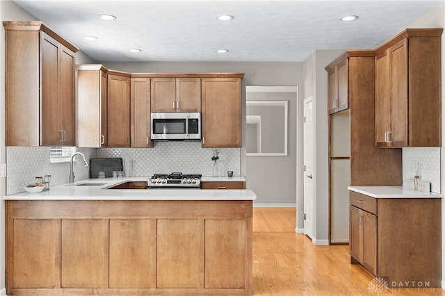 kitchen with light countertops, stainless steel microwave, a sink, and a peninsula