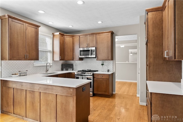 kitchen with stainless steel appliances, a peninsula, a sink, light wood-style floors, and tasteful backsplash