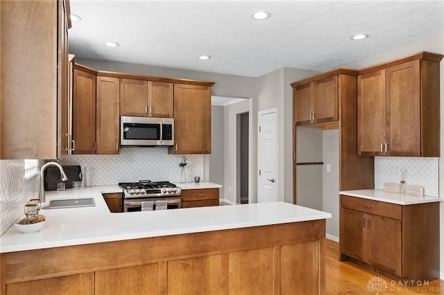 kitchen featuring light wood-style flooring, appliances with stainless steel finishes, brown cabinets, and a sink