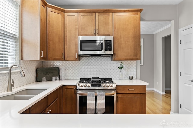 kitchen with stainless steel appliances, a sink, light wood-style floors, light countertops, and tasteful backsplash