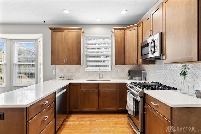 kitchen featuring light wood finished floors, stainless steel appliances, light countertops, a sink, and a peninsula