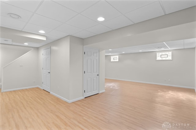 basement featuring light wood-style floors, a drop ceiling, and baseboards