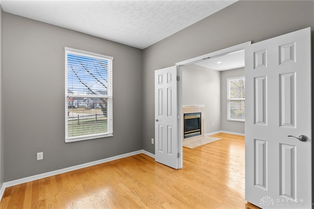 interior space with baseboards, a textured ceiling, a tiled fireplace, and light wood-style floors