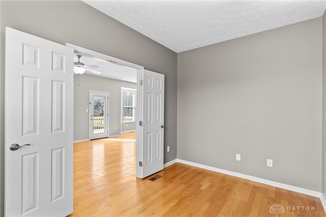 unfurnished room featuring a textured ceiling, ceiling fan, light wood-style flooring, visible vents, and baseboards