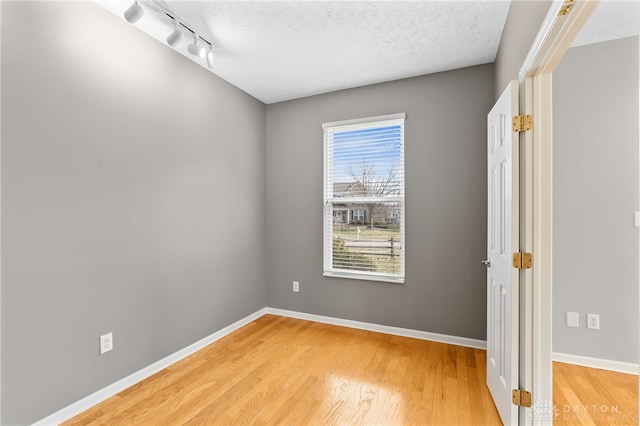 unfurnished room with light wood-style floors, track lighting, a textured ceiling, and baseboards