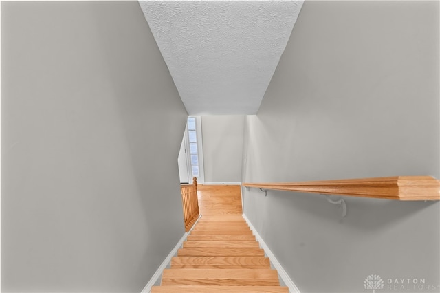 staircase featuring a textured ceiling, wood finished floors, and baseboards