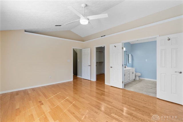 unfurnished bedroom featuring ensuite bathroom, vaulted ceiling, a closet, light wood-type flooring, and a walk in closet