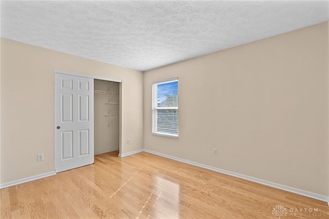 unfurnished bedroom featuring light wood-type flooring, a closet, baseboards, and a textured ceiling