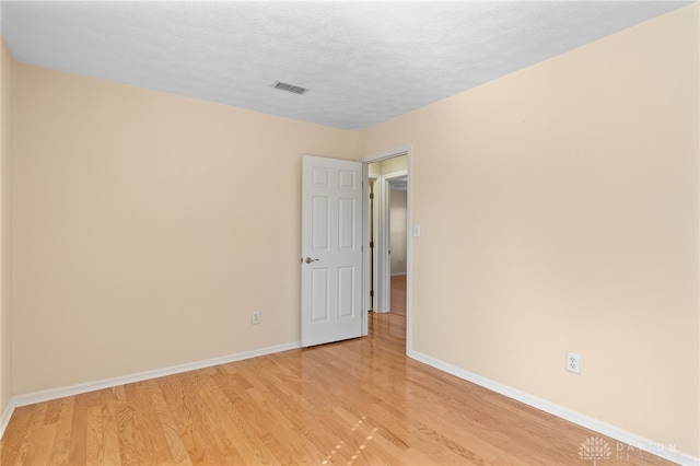 spare room with light wood-type flooring, visible vents, a textured ceiling, and baseboards