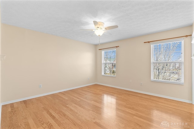 spare room featuring light wood-style floors, ceiling fan, baseboards, and a textured ceiling