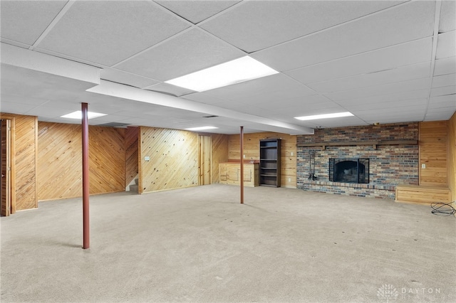 finished basement with a paneled ceiling, a fireplace, wood walls, and carpet flooring