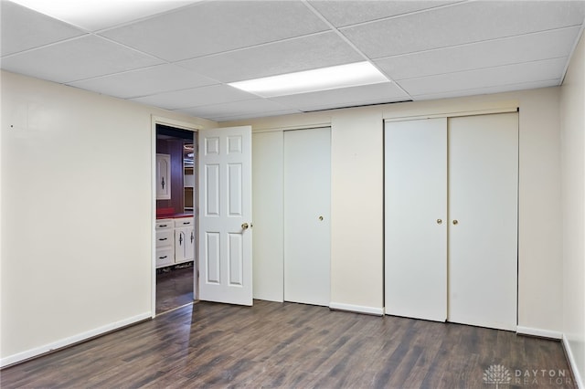 unfurnished bedroom with a paneled ceiling, multiple closets, baseboards, and wood finished floors