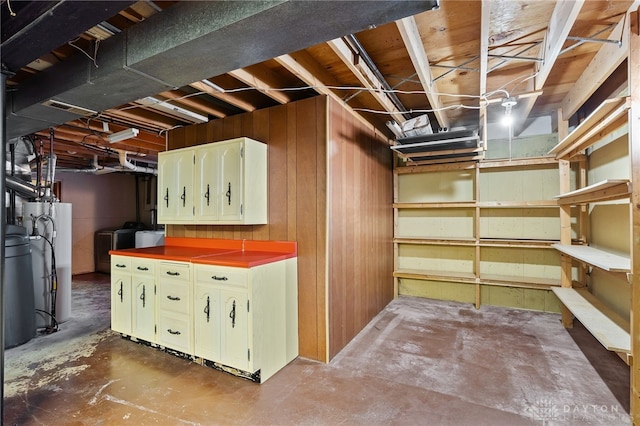 unfinished basement featuring water heater, wooden walls, and washer / clothes dryer