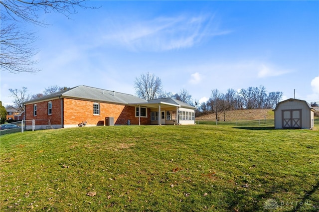 back of property featuring a sunroom, an outbuilding, fence, a storage unit, and brick siding