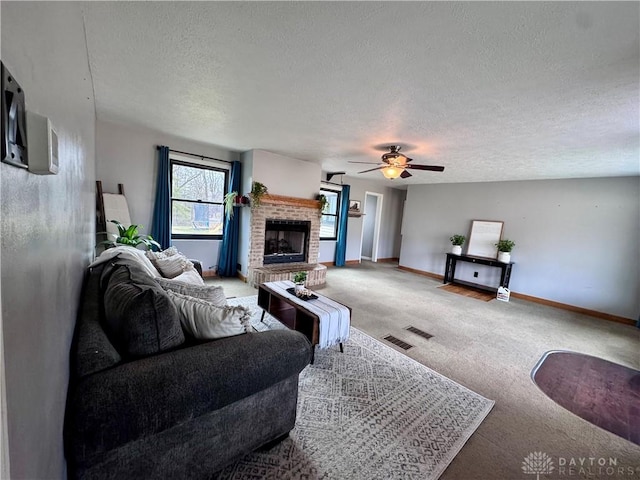 living room featuring baseboards, ceiling fan, a textured ceiling, carpet flooring, and a brick fireplace