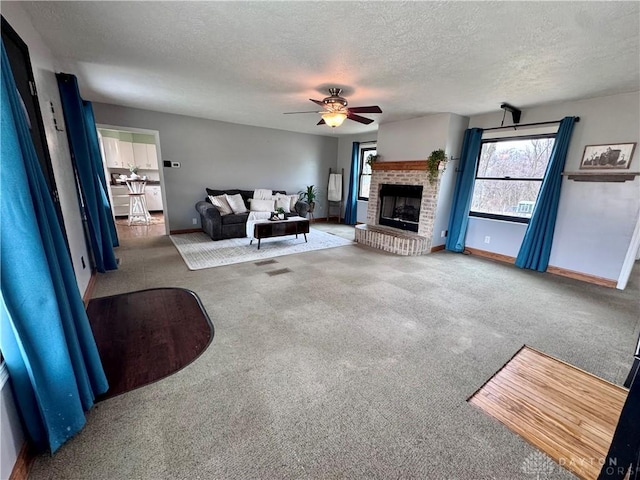 carpeted living room featuring ceiling fan, a fireplace, baseboards, and a textured ceiling