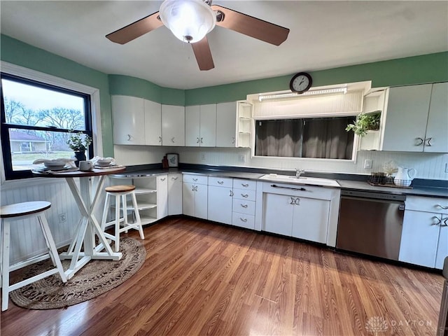 kitchen with dark countertops, wood finished floors, stainless steel dishwasher, open shelves, and a sink