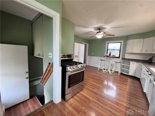 kitchen featuring white refrigerator with ice dispenser, white cabinetry, wainscoting, stainless steel gas stove, and light wood finished floors