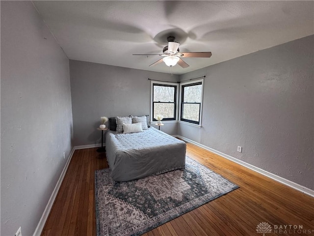 bedroom with a textured wall, hardwood / wood-style floors, a ceiling fan, and baseboards