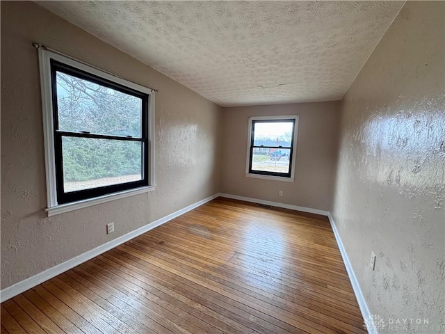 spare room featuring a textured ceiling, a textured wall, hardwood / wood-style flooring, visible vents, and baseboards