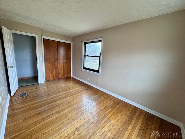 unfurnished bedroom with a closet, baseboards, visible vents, and hardwood / wood-style floors