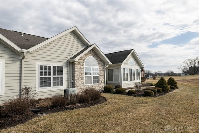 view of side of home with a yard, roof with shingles, stone siding, and cooling unit