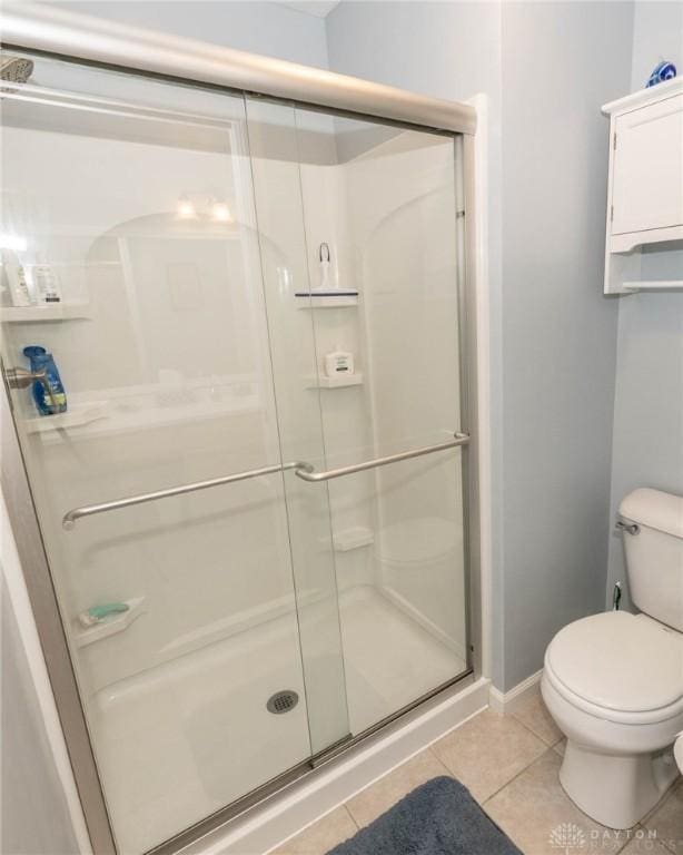 bathroom featuring toilet, a stall shower, tile patterned flooring, and baseboards