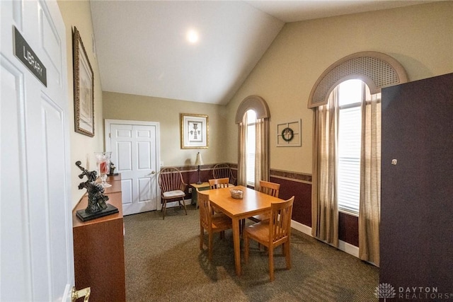 dining space featuring lofted ceiling, a wainscoted wall, and dark carpet