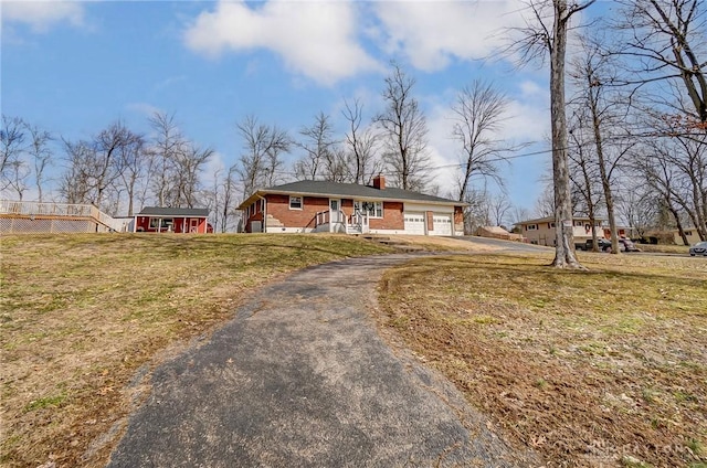 view of front of home with driveway, brick siding, a chimney, an attached garage, and a front yard