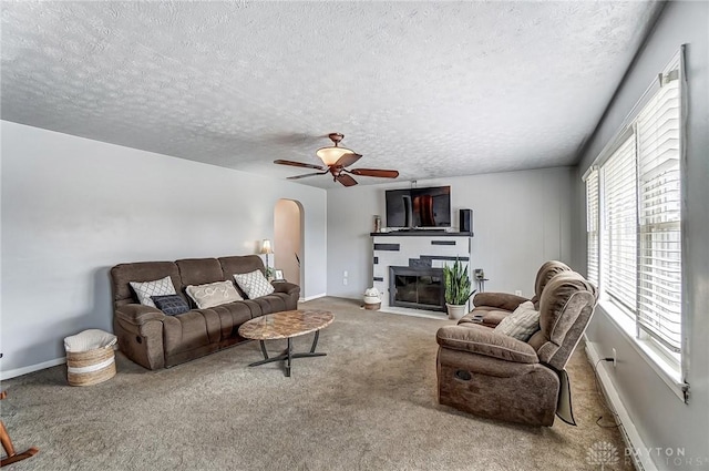 living area with carpet floors, arched walkways, a glass covered fireplace, ceiling fan, and a textured ceiling