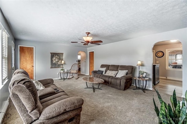 carpeted living area featuring arched walkways, a baseboard heating unit, and a textured ceiling