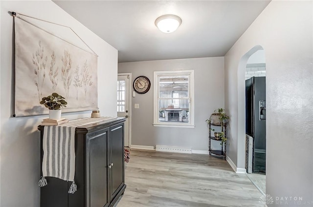 entrance foyer with a baseboard heating unit, light wood finished floors, arched walkways, and baseboards