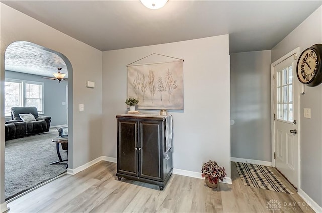 foyer entrance with light wood-style flooring, arched walkways, ceiling fan, and baseboards