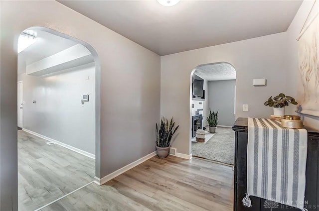 hallway featuring arched walkways, baseboards, and light wood finished floors