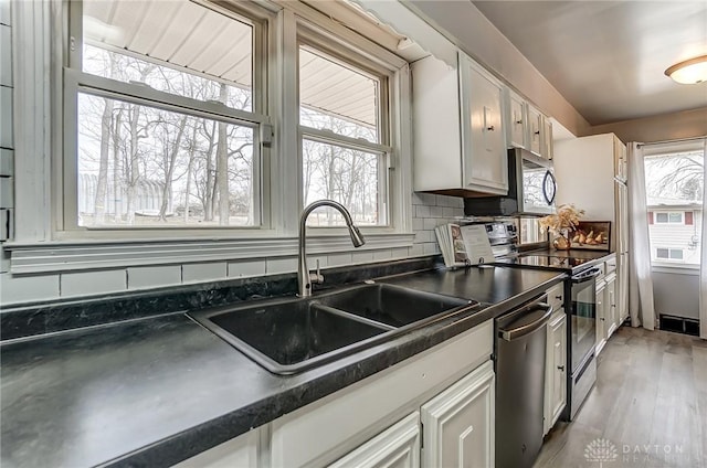 kitchen with a sink, visible vents, appliances with stainless steel finishes, tasteful backsplash, and dark countertops