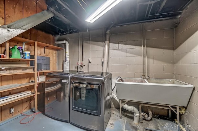 laundry room featuring concrete block wall, laundry area, washing machine and dryer, and a sink