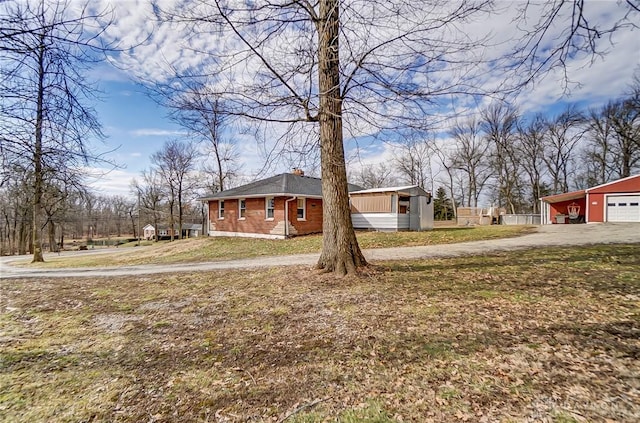 view of side of property featuring driveway, a chimney, a detached garage, a yard, and brick siding