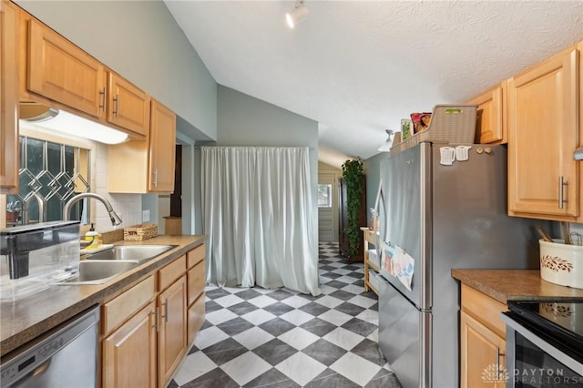 kitchen with lofted ceiling, stainless steel appliances, light brown cabinetry, light floors, and a sink