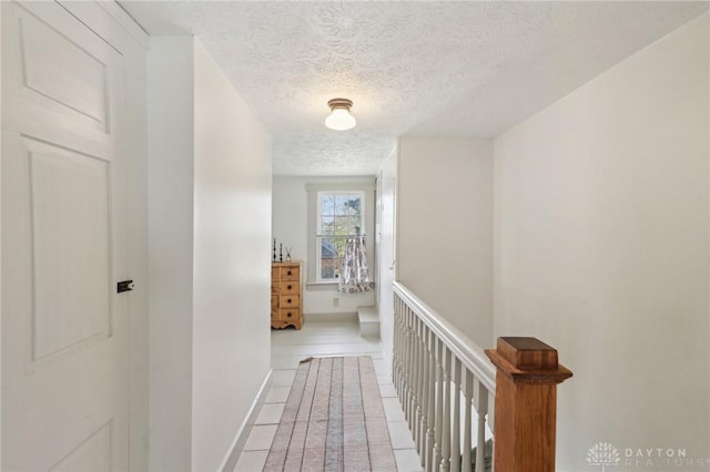 hallway with baseboards, a textured ceiling, an upstairs landing, and light tile patterned floors