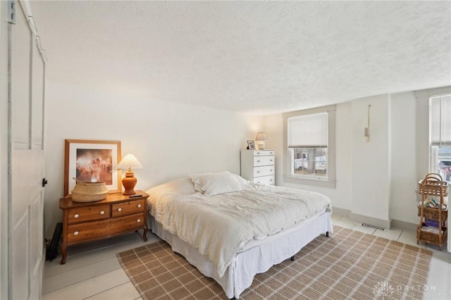 bedroom featuring a textured ceiling, light tile patterned floors, visible vents, and baseboards